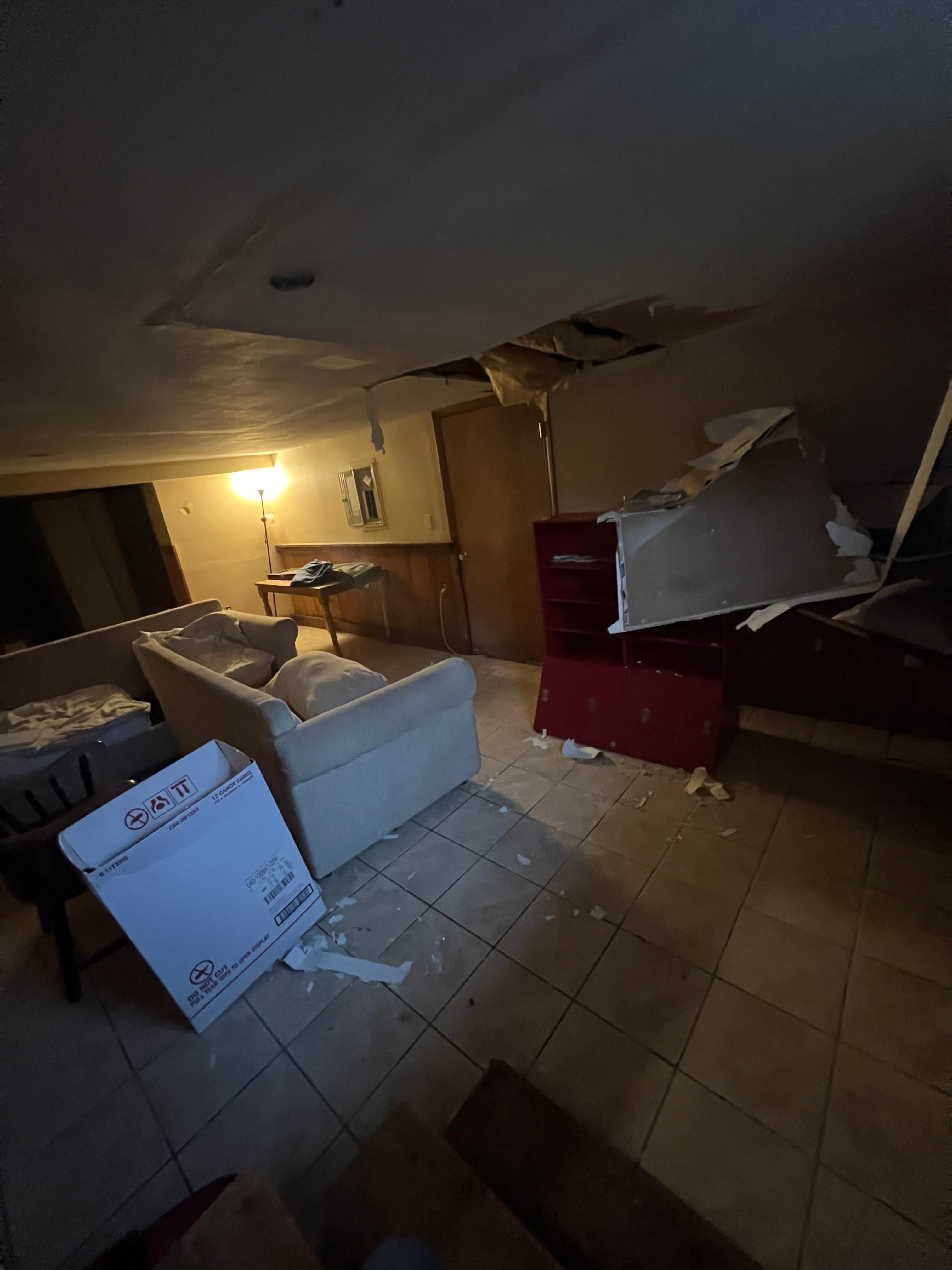 Collapsed ceiling with debris scattered over a white sofa and red cabinet in a room.