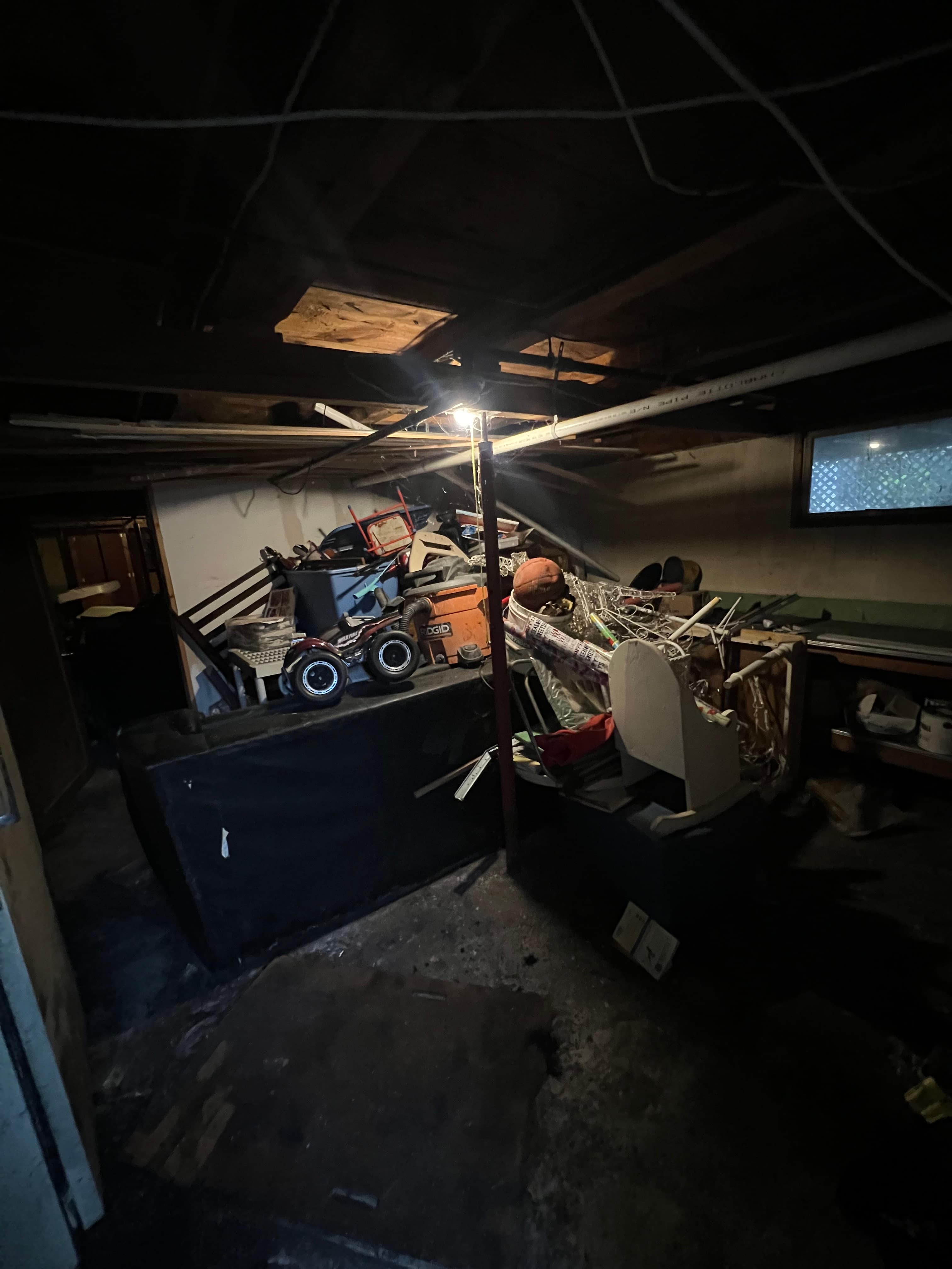 Cluttered, dimly lit basement storage area filled with miscellaneous items, toys, and tools.