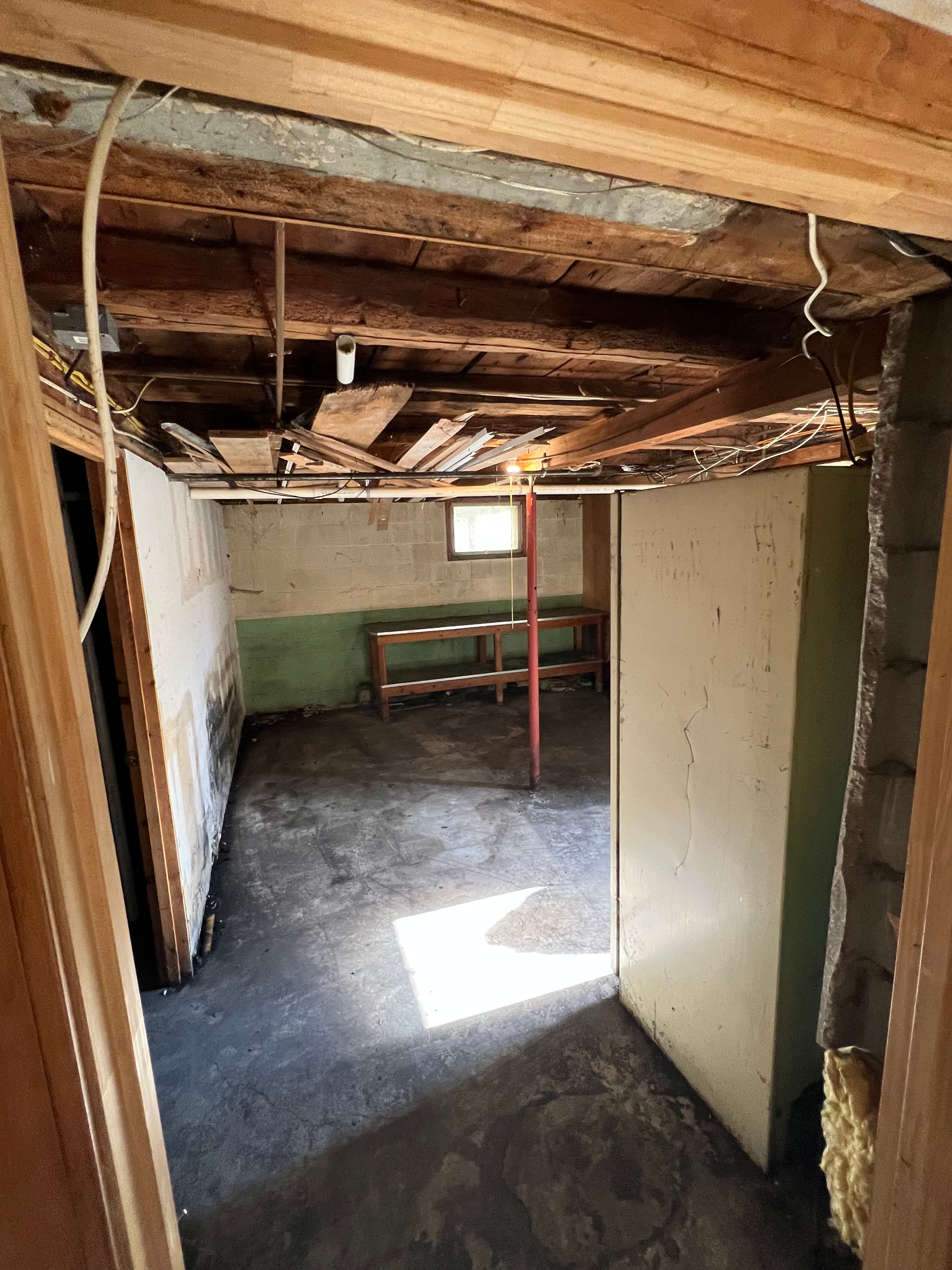 Unfinished basement with exposed wooden ceiling joists, concrete floor, and a wooden workbench.