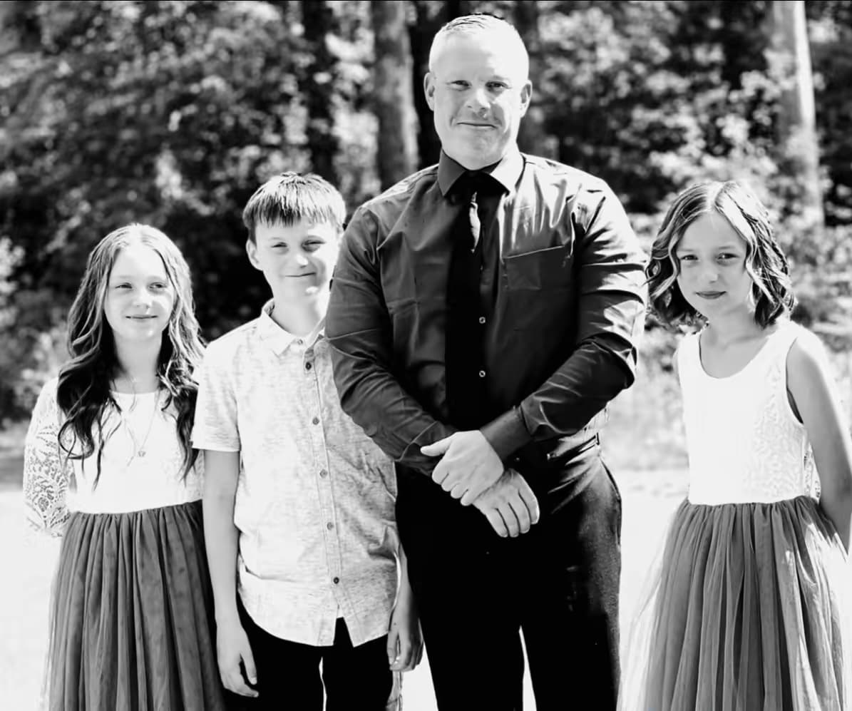 Black and white portrait of a man and three children smiling in formal outdoor attire.